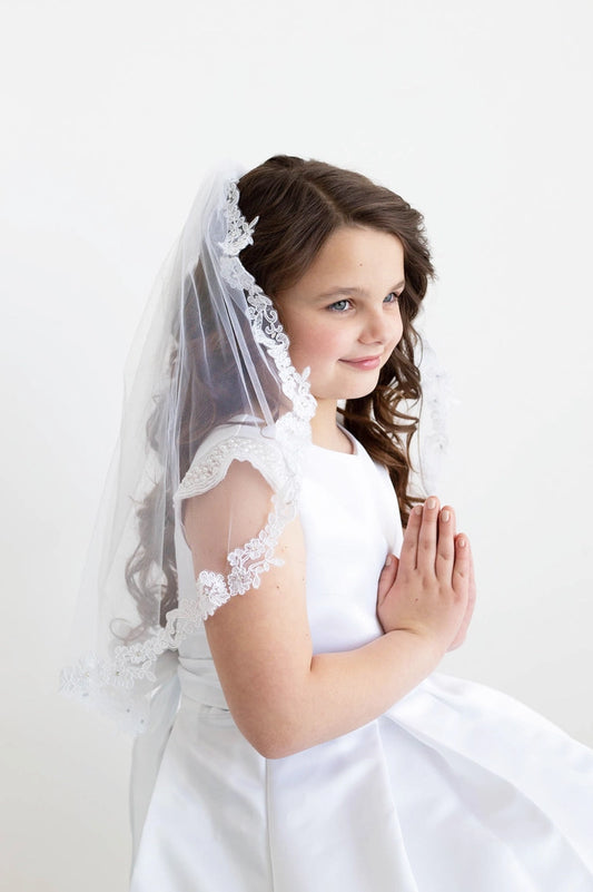 Young girl in a white dress with a lace veil against a white background