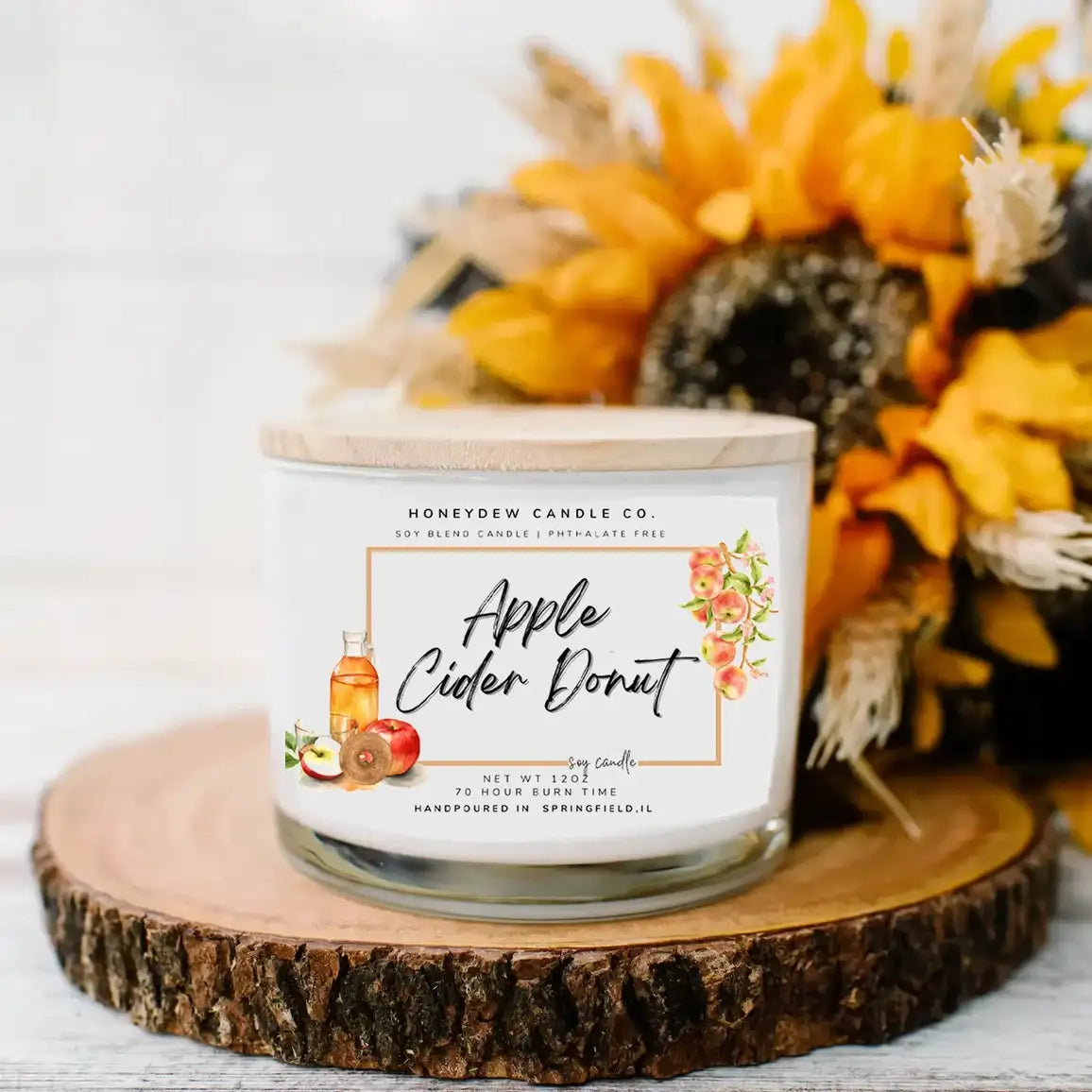 Candle labeled 'Apple Cider Donut' from Honeydew Candle Co. on a wooden surface with decorative fall elements.