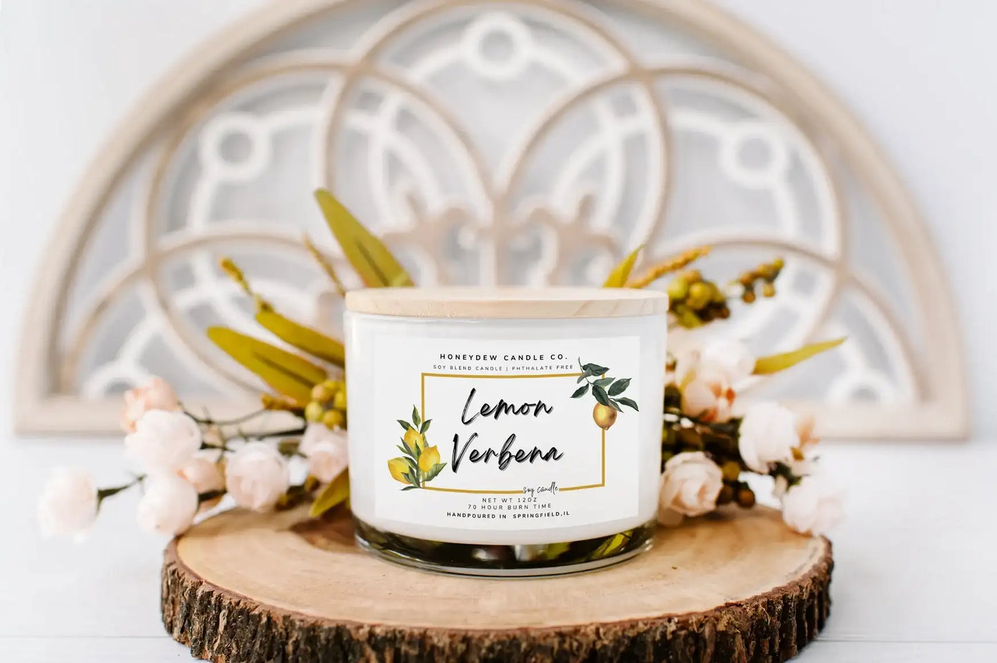 Candle labeled 'Lemon Verbena' on a wooden coaster with decorative elements in the background