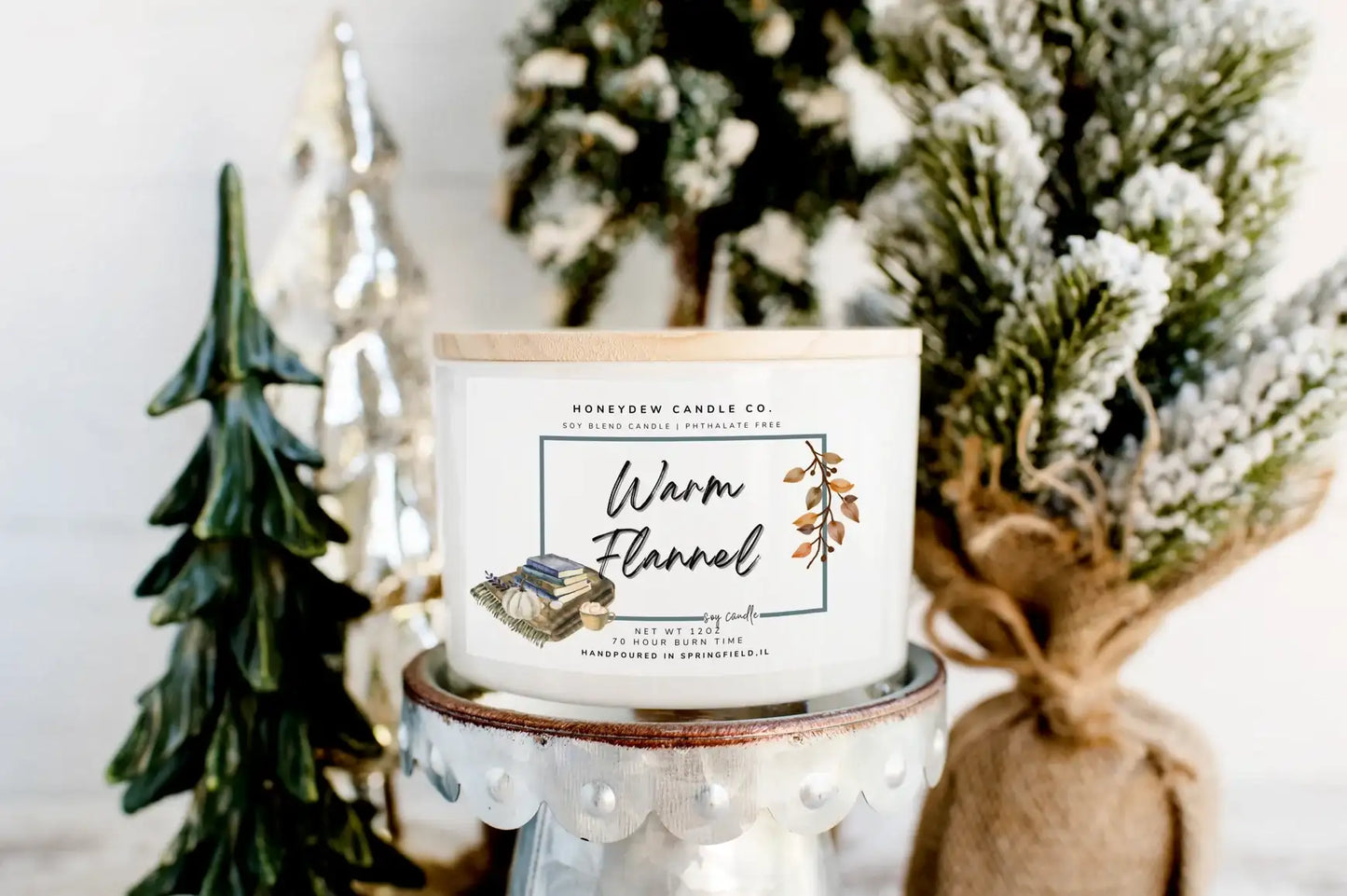 Candle with a label in front of decorative Christmas trees
