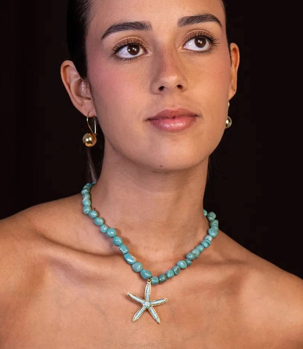 Woman wearing a turquoise necklace with a starfish pendant against a dark background