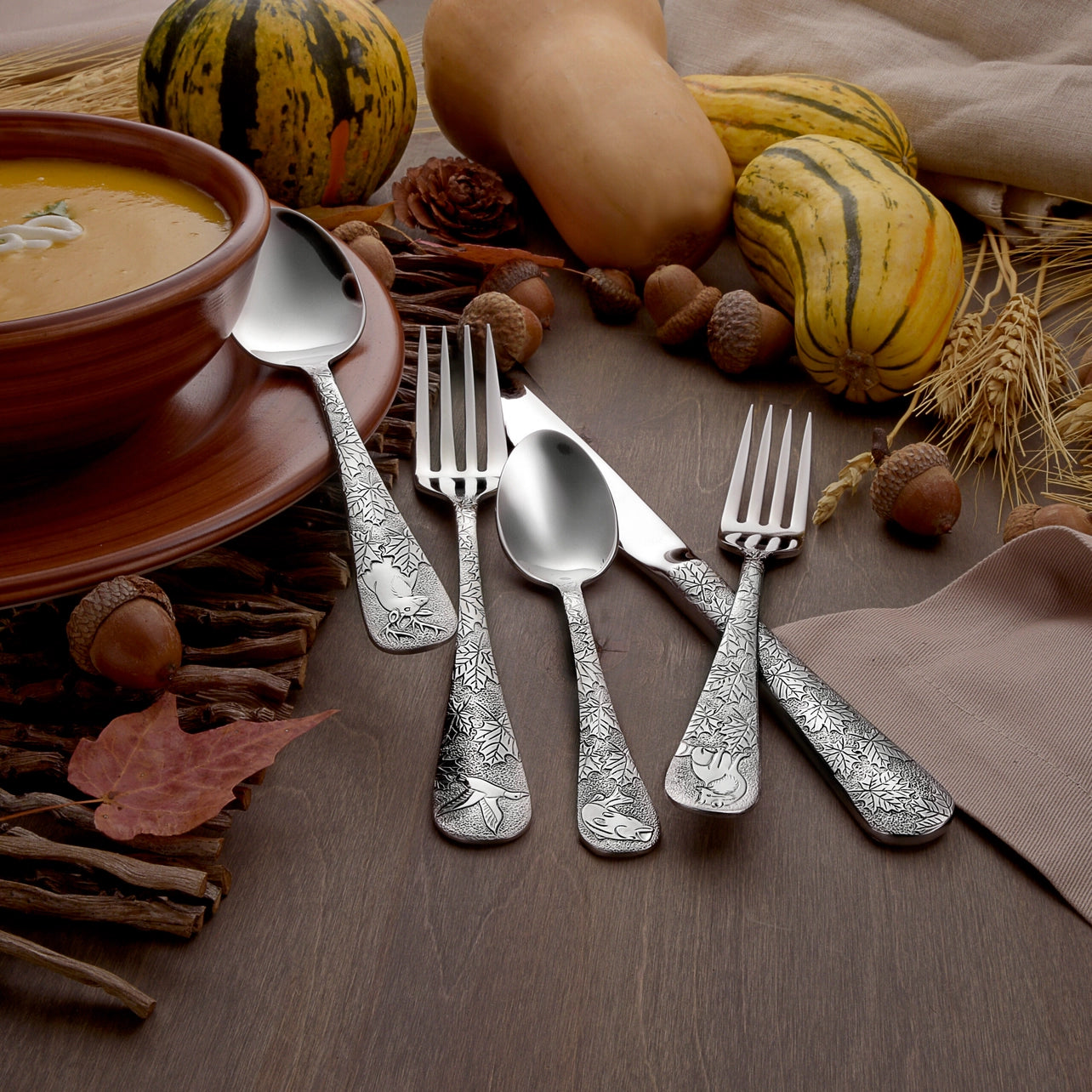 Silver cutlery set on a wooden surface with pumpkins and soup bowl in the background