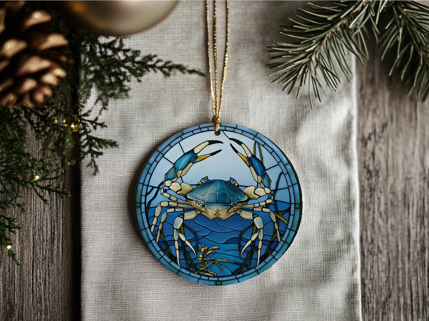 Decorative ornament with blue crab design on a wooden surface with pine branches.