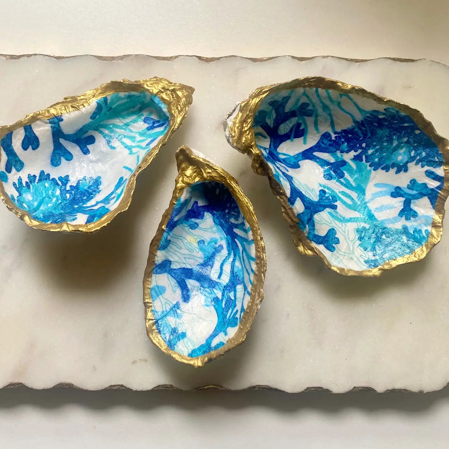 Three decorative oyster shells with blue reef patterns on a marble surface