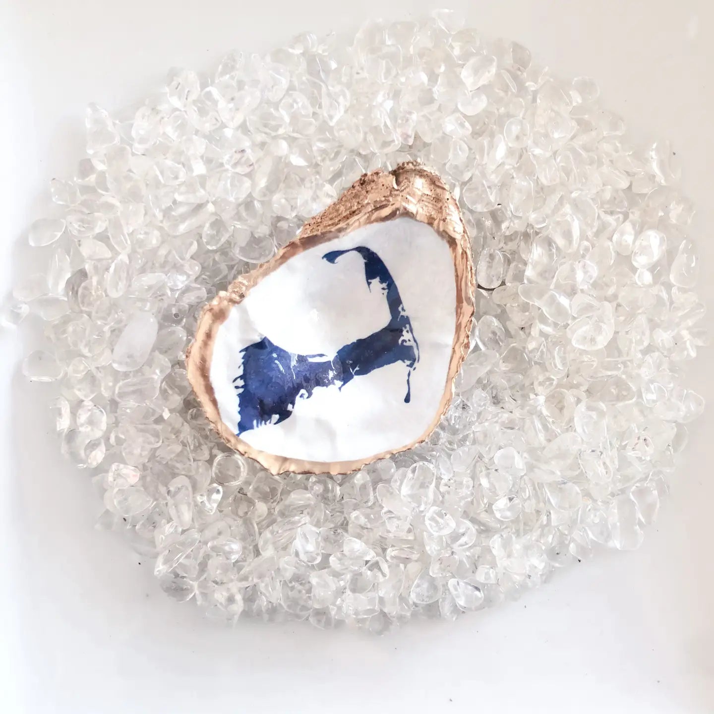 Decorative oyster shell with blue interior of a map of cape Cod on a bed of clear pebbles