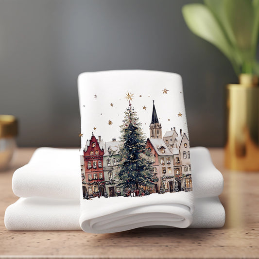 Folded white towel with a Christmas-themed design of a town and tree on a wooden surface.