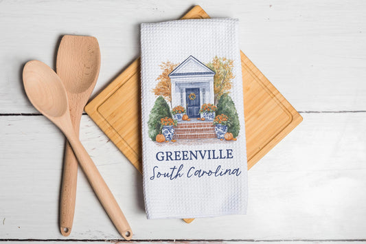 Kitchen towel with Greenville, South Carolina design on a wooden cutting board with utensils.