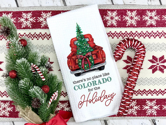 Decorative towel with Christmas tree and red truck design, placed on a festive mat with candy cane and tree.