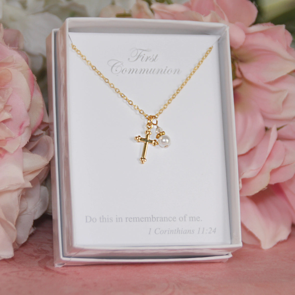 Gold necklace with a cross and pearl pendant in a box with pink flowers in the background