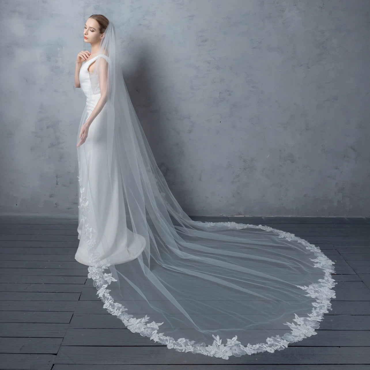 Woman wearing a white wedding dress with a long veil against a gray background