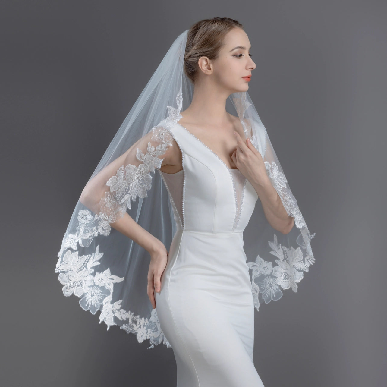 Woman wearing a white wedding dress with a lace veil against a gray background
