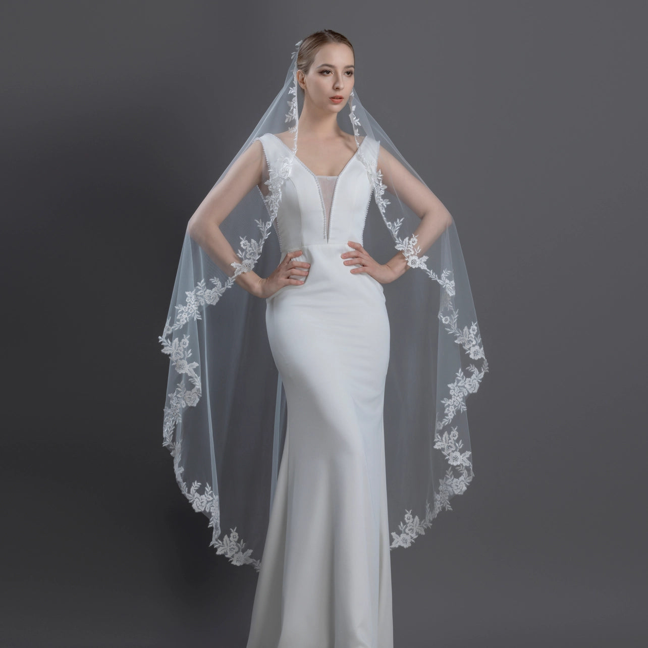 Woman wearing an ivory mantilla wedding dress with a long veil on a dark background