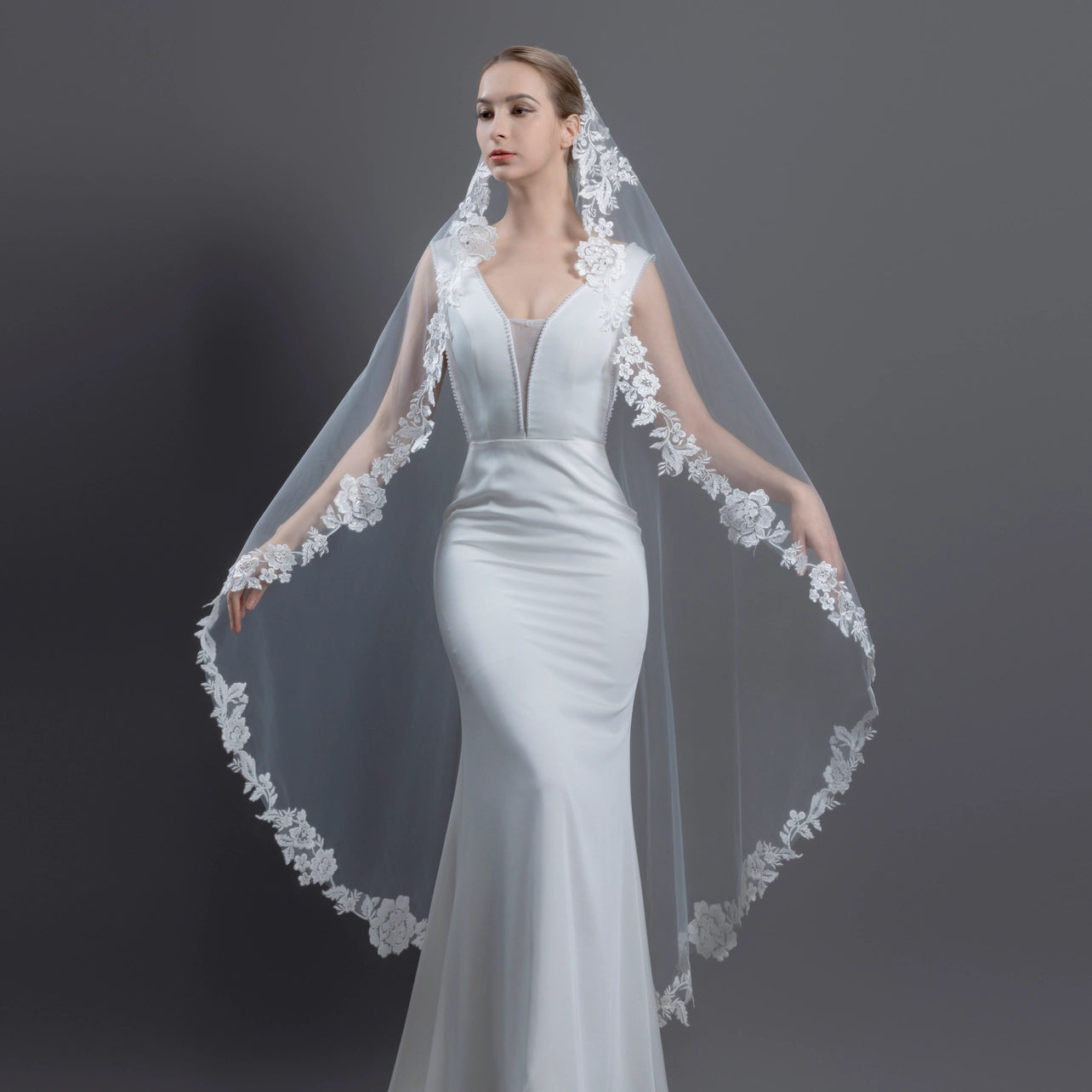 Woman wearing a white wedding dress with an intricate lace veil against a dark background