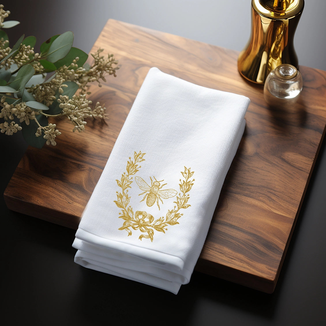 White towel with gold bee design on a wooden surface with decorative elements.