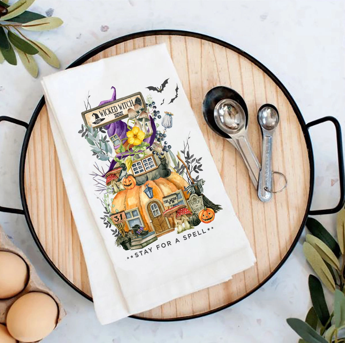 Halloween-themed kitchen towel on a wooden board with measuring spoons and eggs.