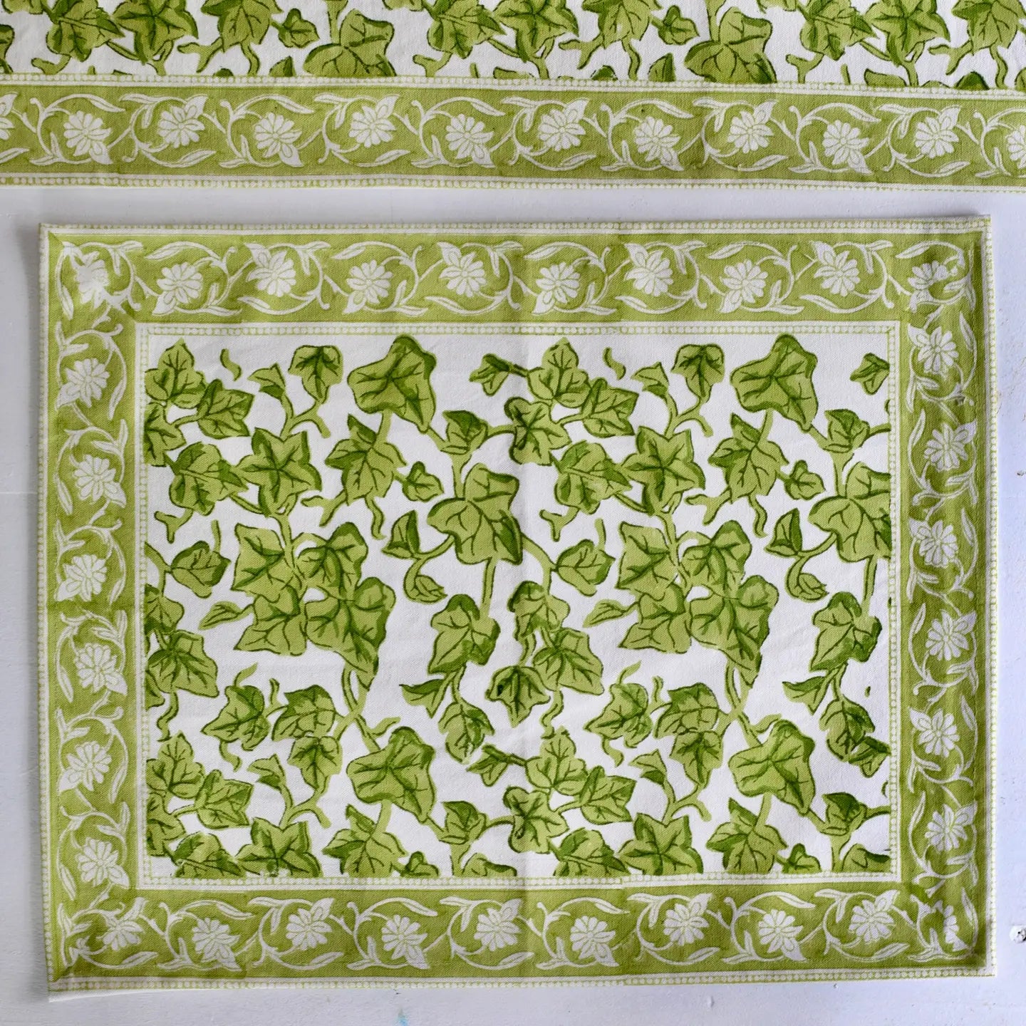 Green leaf patterned fabric with white floral border on a white background