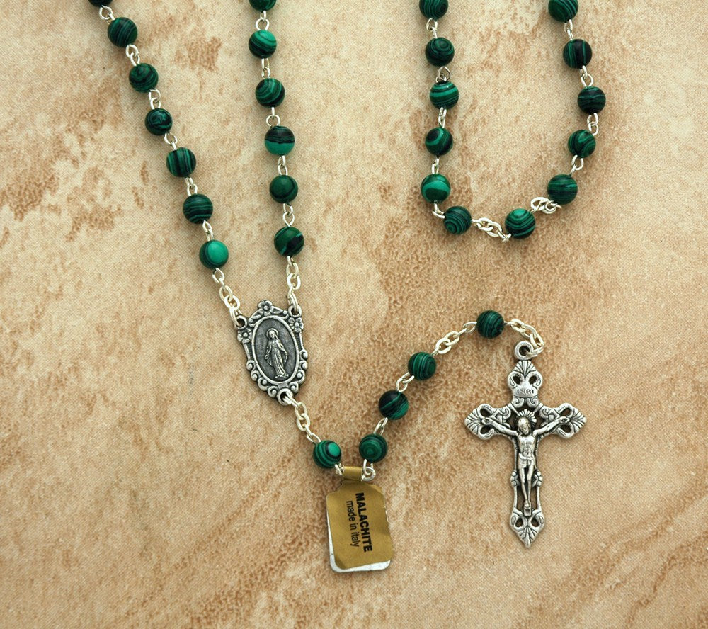 Green rosary with silver crucifix and medal on a beige background