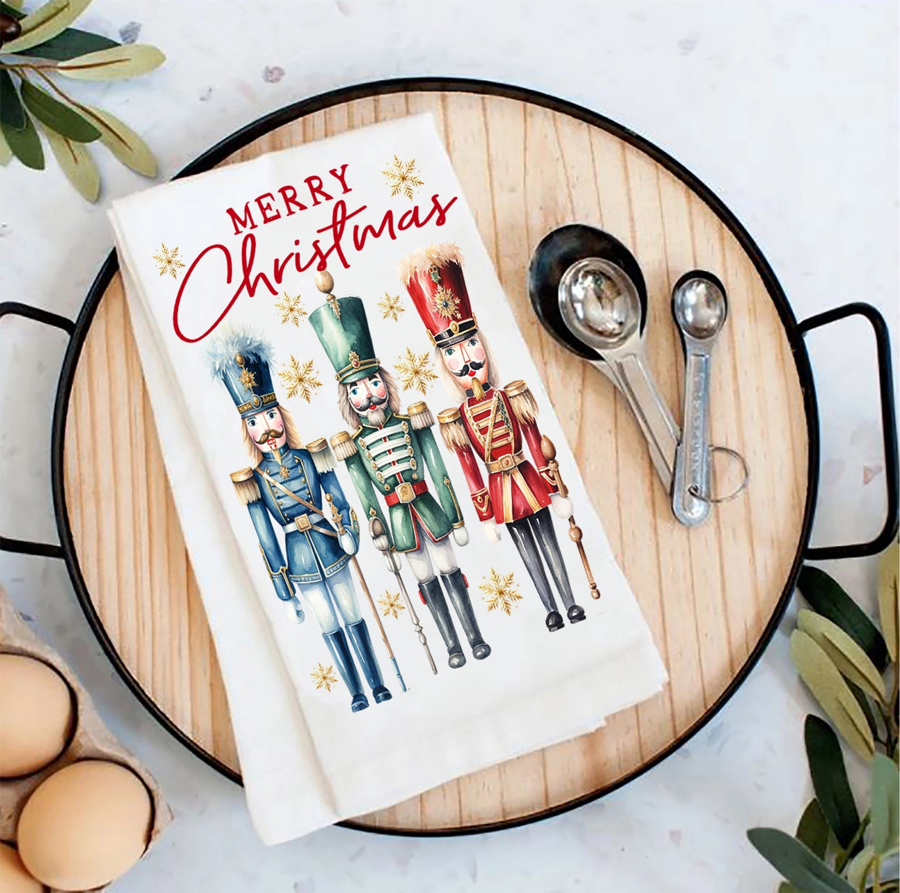 Christmas-themed kitchen towel with nutcrackers on a wooden board with measuring spoons and eggs.