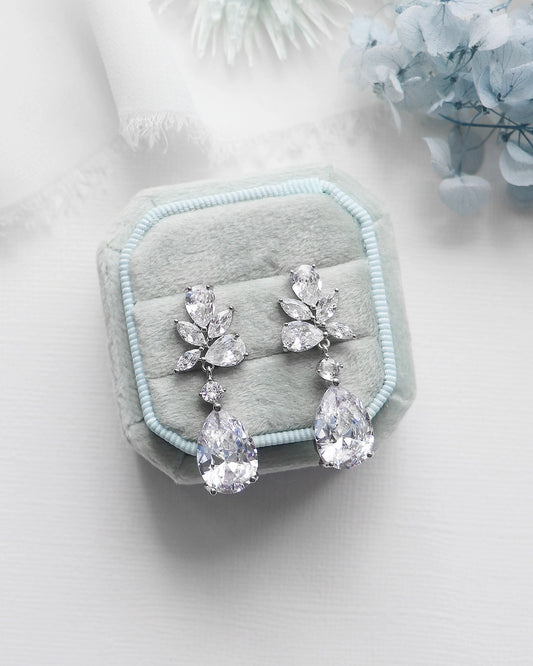 Pair of silver teardrop earrings on a light blue cushion with a soft white background