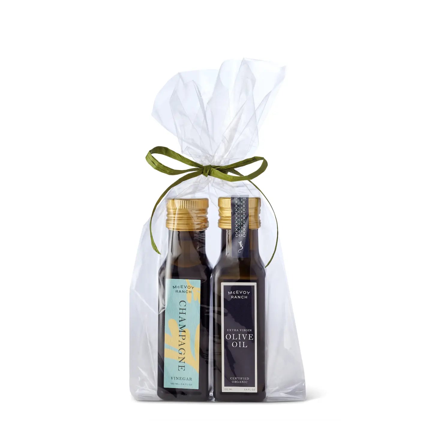 Two bottles of champagne and olive oil in a clear gift bag with a green ribbon on a white background.