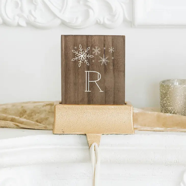 Decorative wooden sign with snowflakes and a letter 'R' on top of a gold ribbon.