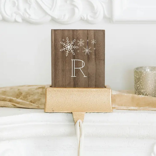 Decorative wooden sign with snowflakes and a letter 'R' on top of a gold ribbon.