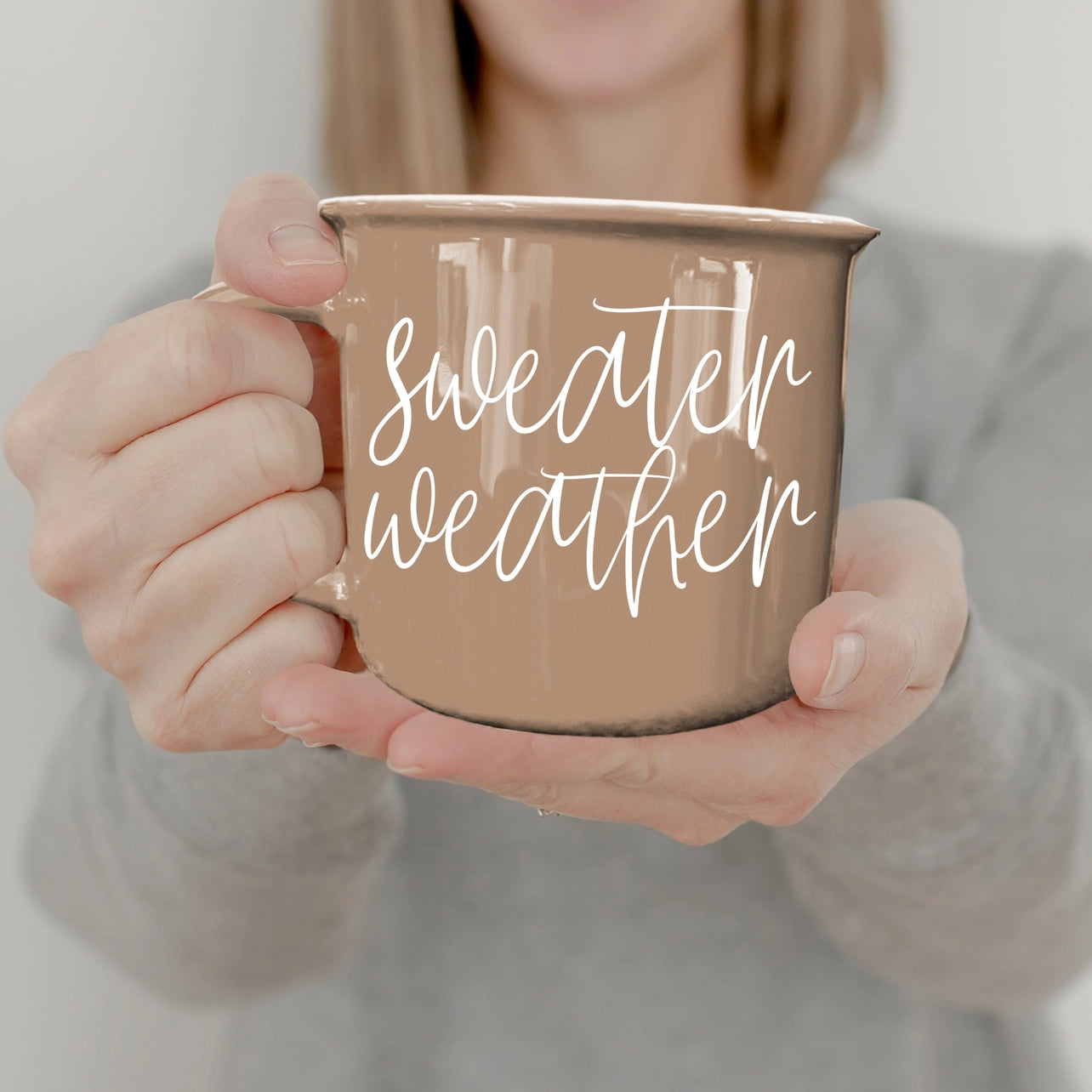 Person holding a mug with 'sweater weather' text against a neutral background