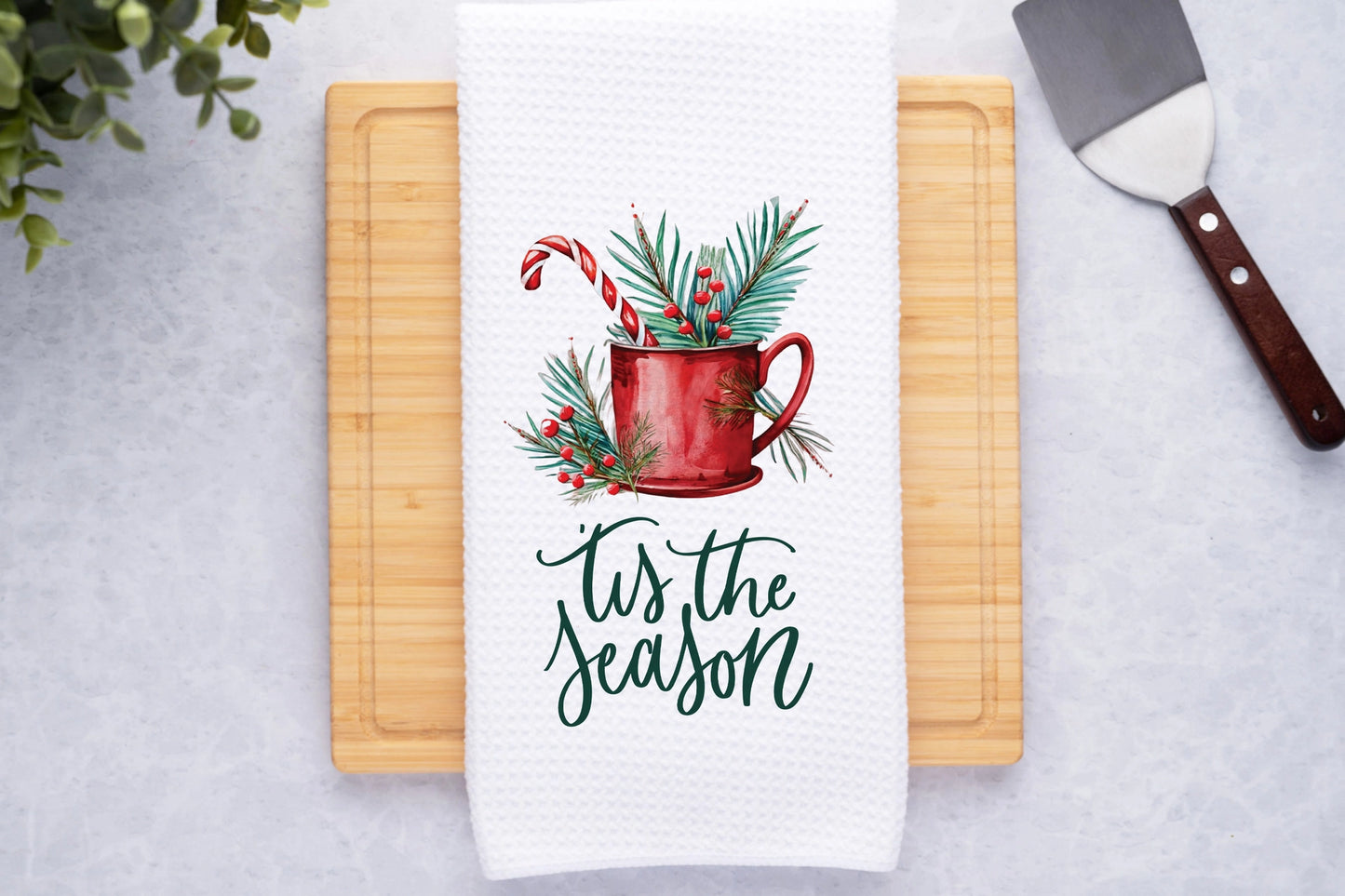 Towel with Christmas design and 'tis the season text on a cutting board.