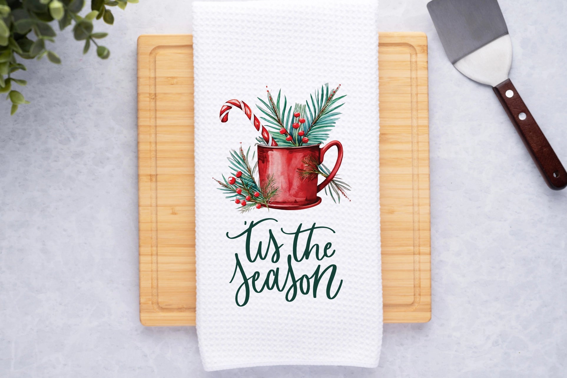 Towel with Christmas design and 'tis the season text on a cutting board.