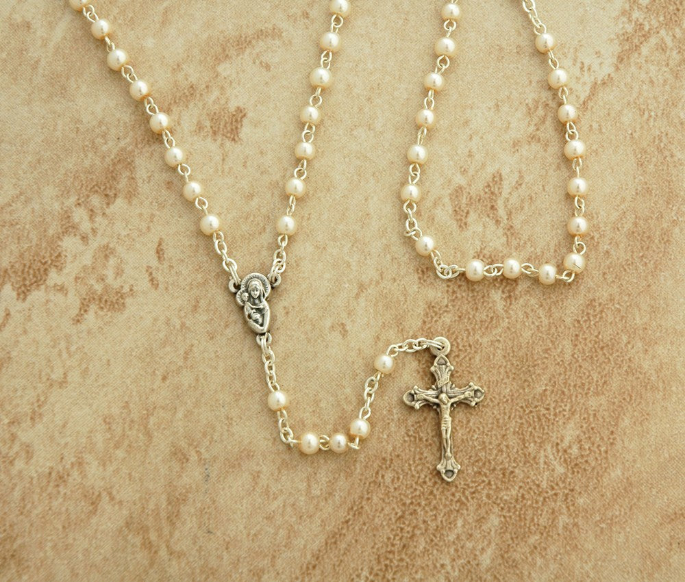 Pearl rosary necklace with a cross on a beige textured background