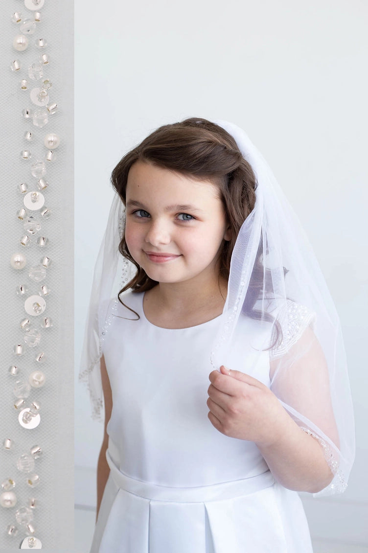 Young girl in a white dress with a veil standing against a white background