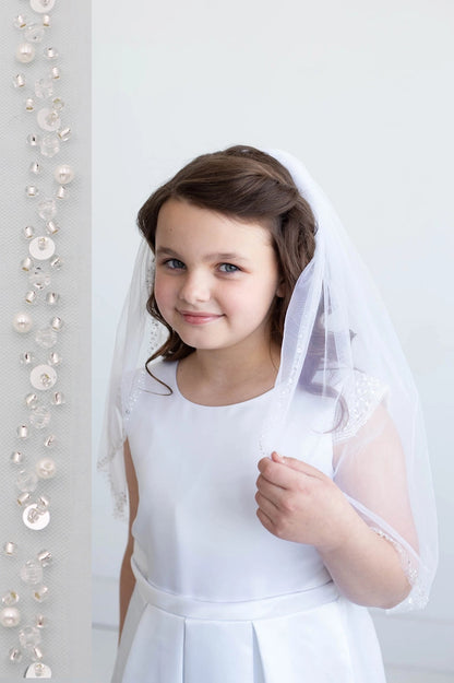 Young girl in a white dress with a veil standing against a white background