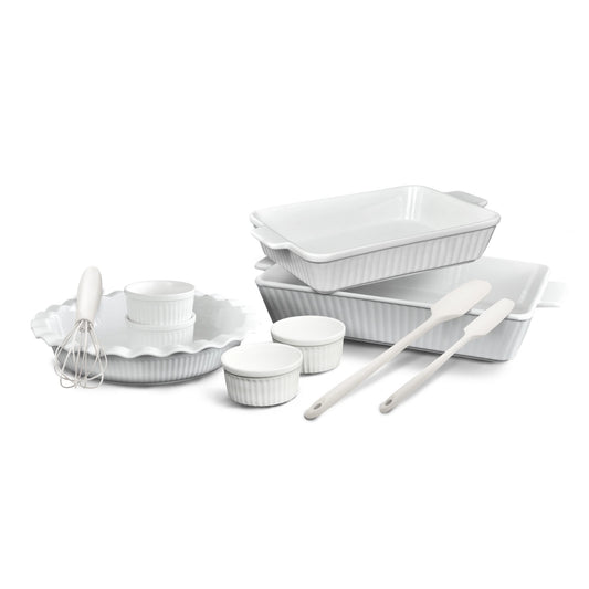 Set of white ceramic cookware including bowls, a whisk, and spatulas on a white background