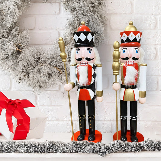 Two nutcrackers in festive attire with a white brick wall and gift box in the background.