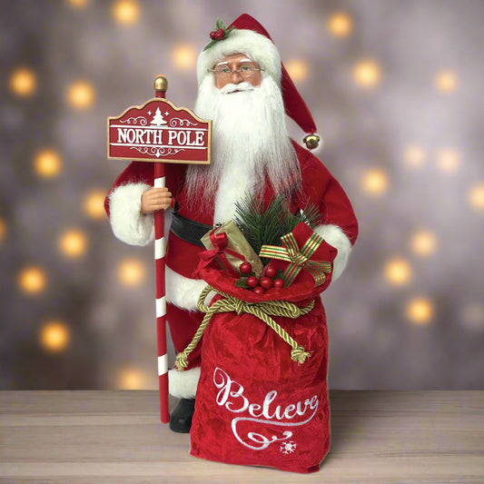Santa Claus figure holding a 'North Pole' sign and a sack with 'Believe' on a white background