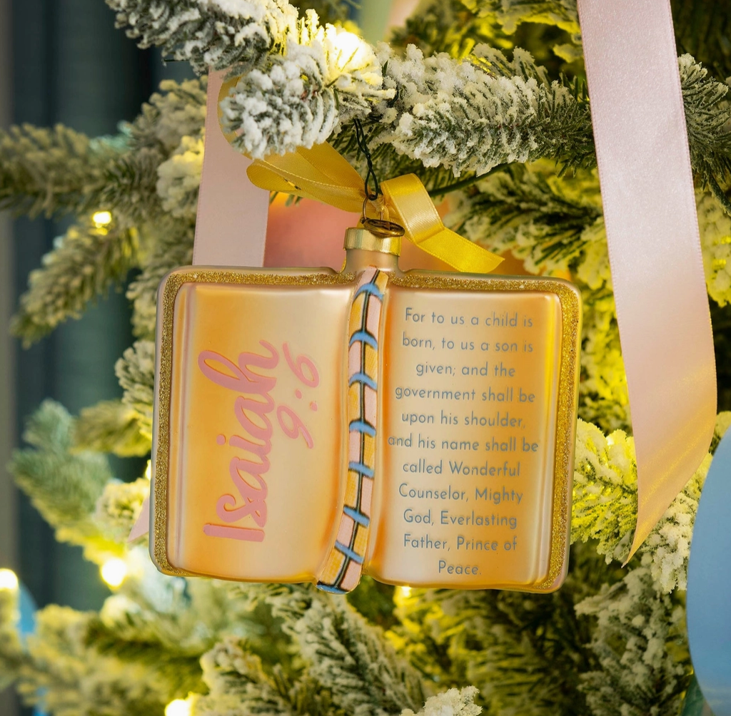 2026 Isaiah 9:6 open Bible blown glass Christmas ornament in gold pink and blue hanging on a flocked Christmas tree
