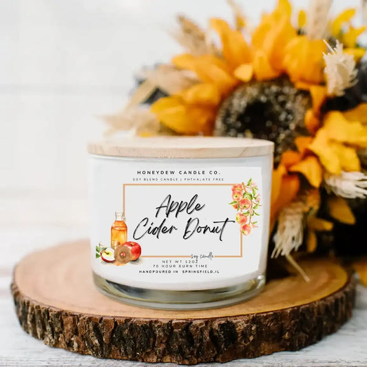 Candle labeled 'Apple Cider Donut' from Honeydew Candle Co. on a wooden surface with decorative fall elements.