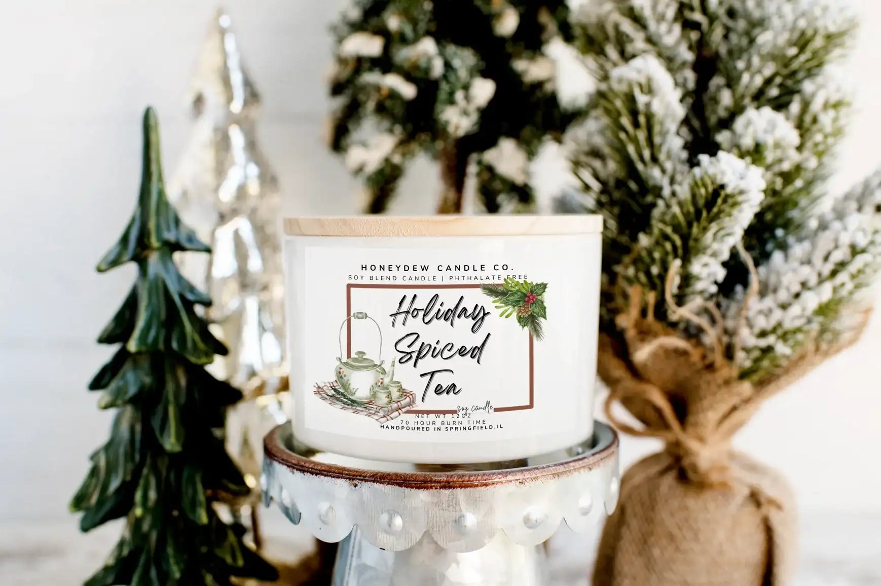 Candle labeled 'Holiday Spiced Tea' with decorative Christmas trees in the background