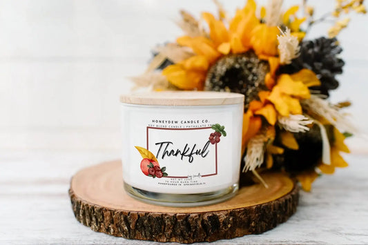 Candle labeled 'Thankful' on a wooden coaster with sunflowers and pinecones.