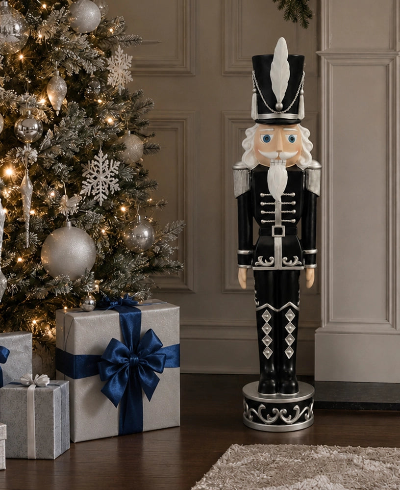 A tall black and silver nutcracker figurine stands beside a decorated Christmas tree and wrapped gift boxes in a holiday indoor setting.