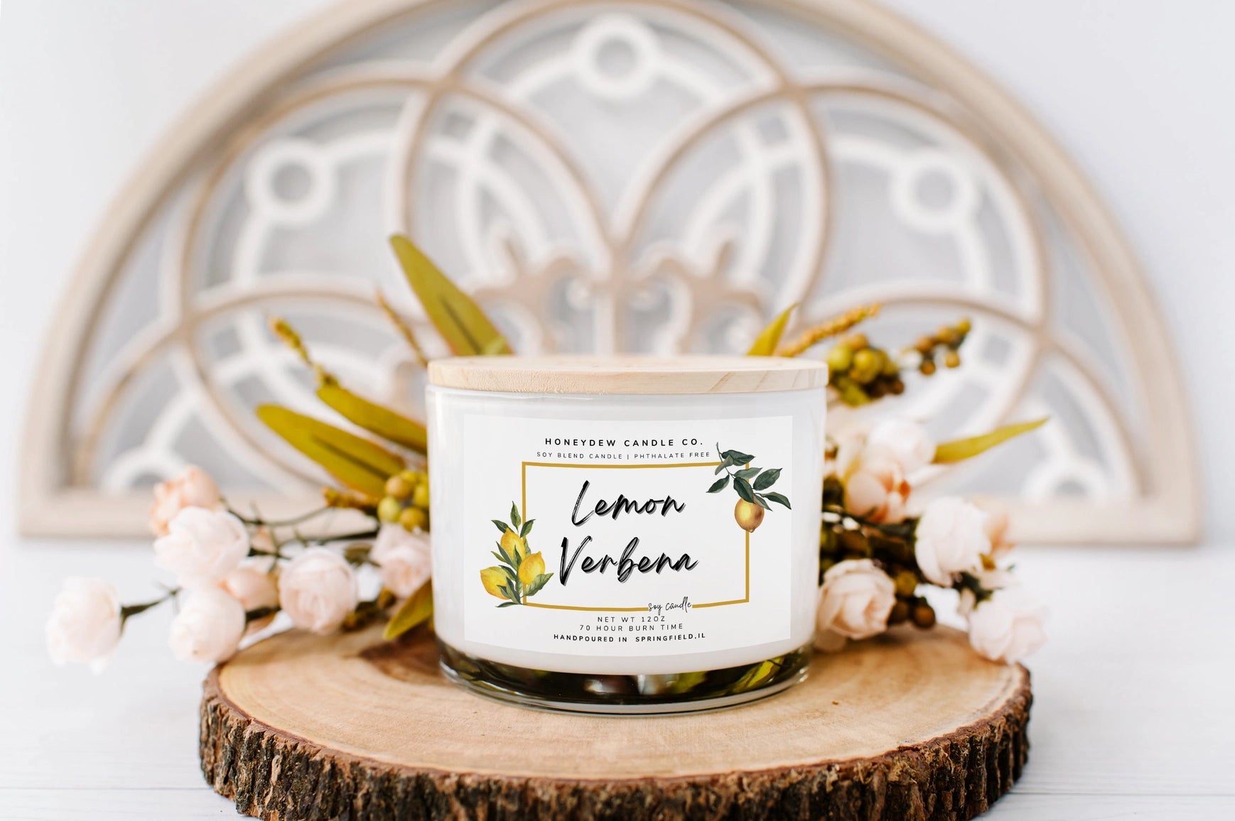 Candle labeled 'Lemon Verbena' on a wooden coaster with decorative elements in the background