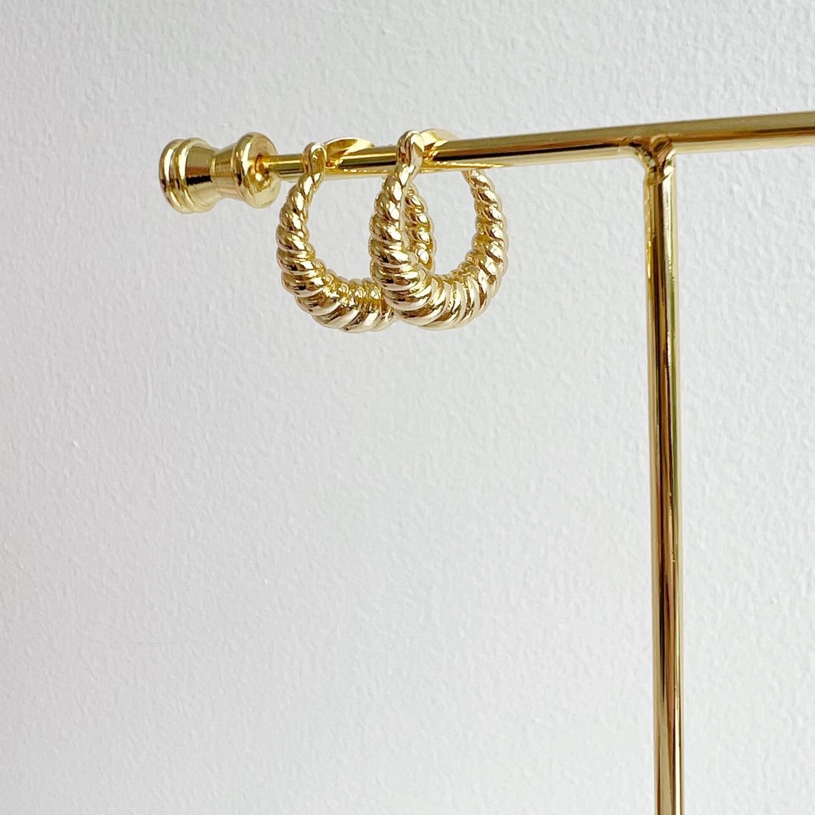 Gold hoop earrings on a gold stand against a white background