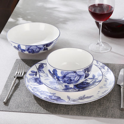 Blue and white floral ceramic dinnerware set on a dining table, including a plate, bowl, and matching cup, styled with silverware, a placemat, and a glass of red wine.