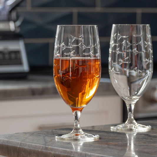 Two glasses, one filled with amber liquid and the other empty, on a kitchen counter.