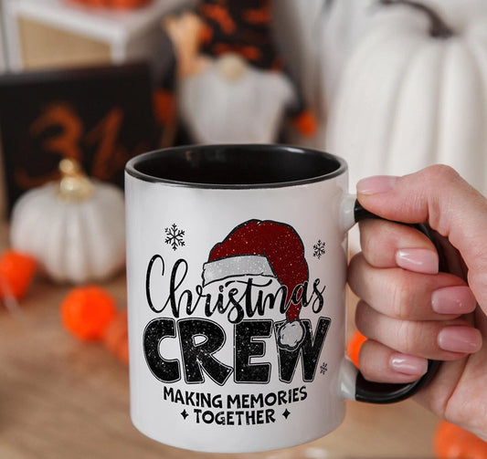 White mug with 'Christmas Crew' design held by a hand, with Halloween decorations in the background.