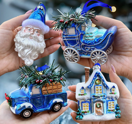 Four Christmas-themed ornaments including a Santa figure, a house, a truck, and a carriage held in hands.
