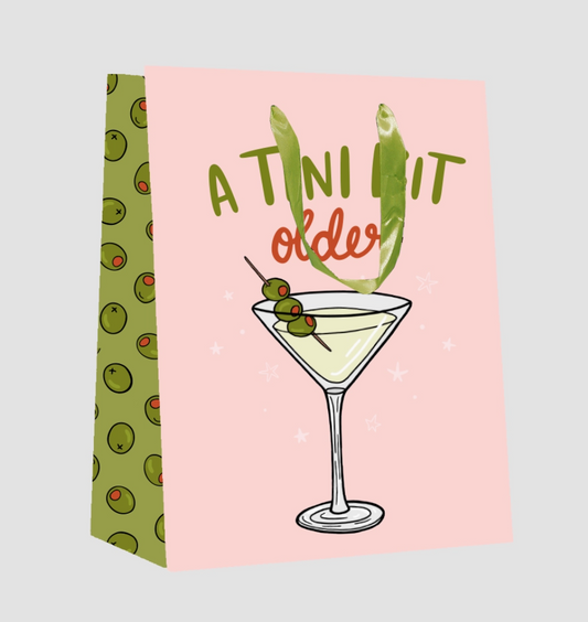Two cocktail-themed towels, one with a martini glass and olives, the other with a humorous text design on a pink background.