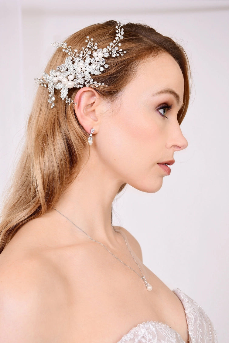 Woman wearing a decorative hairpiece with pearls and flowers on a plain background