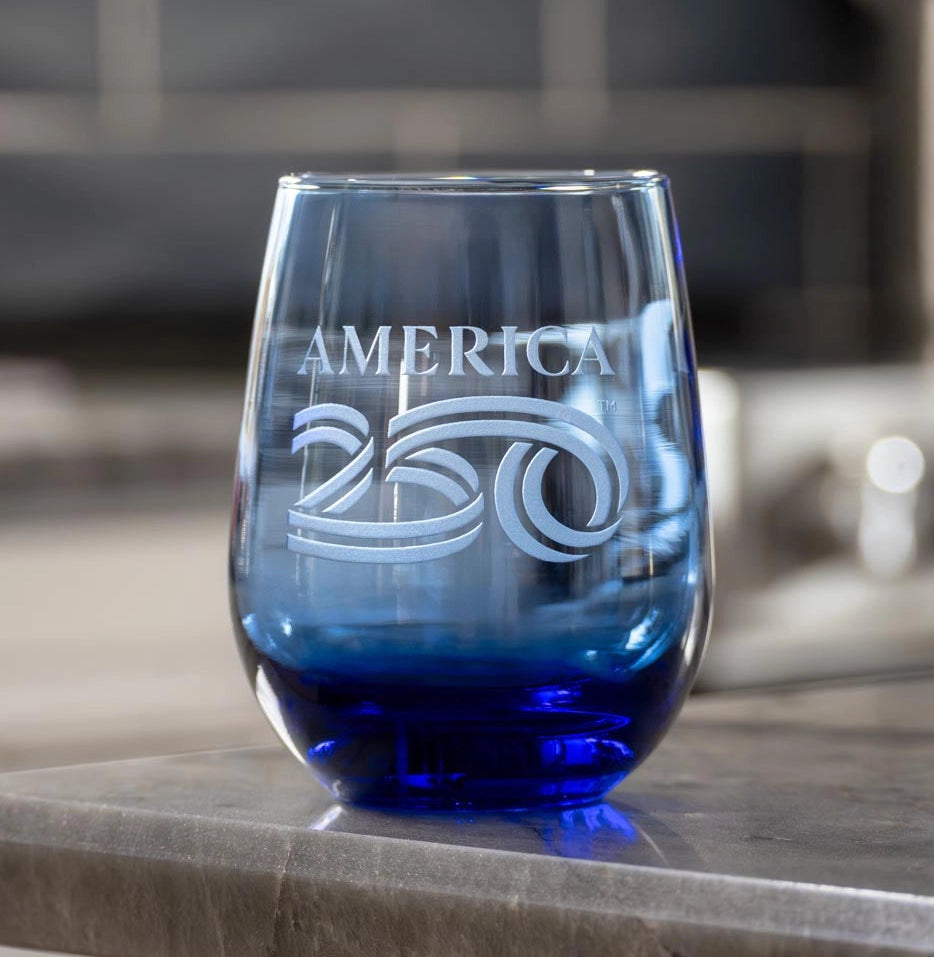 Blue wine glass with 'AMERICA 250' engraving on a stone surface