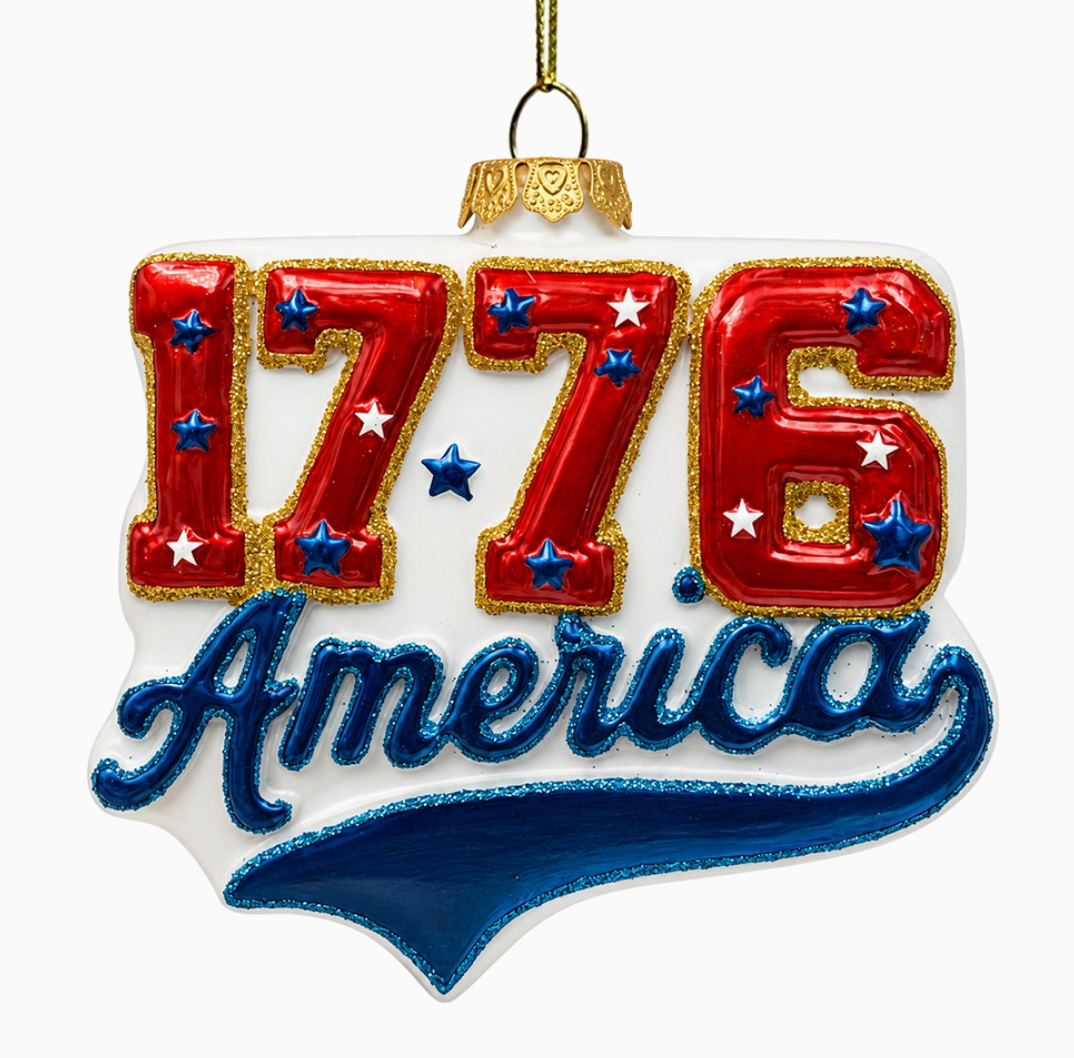 America 1776 patriotic hand-blown glass ornament with red 1776 numbers, blue America lettering, stars and gold accents for the USA 250th anniversary.